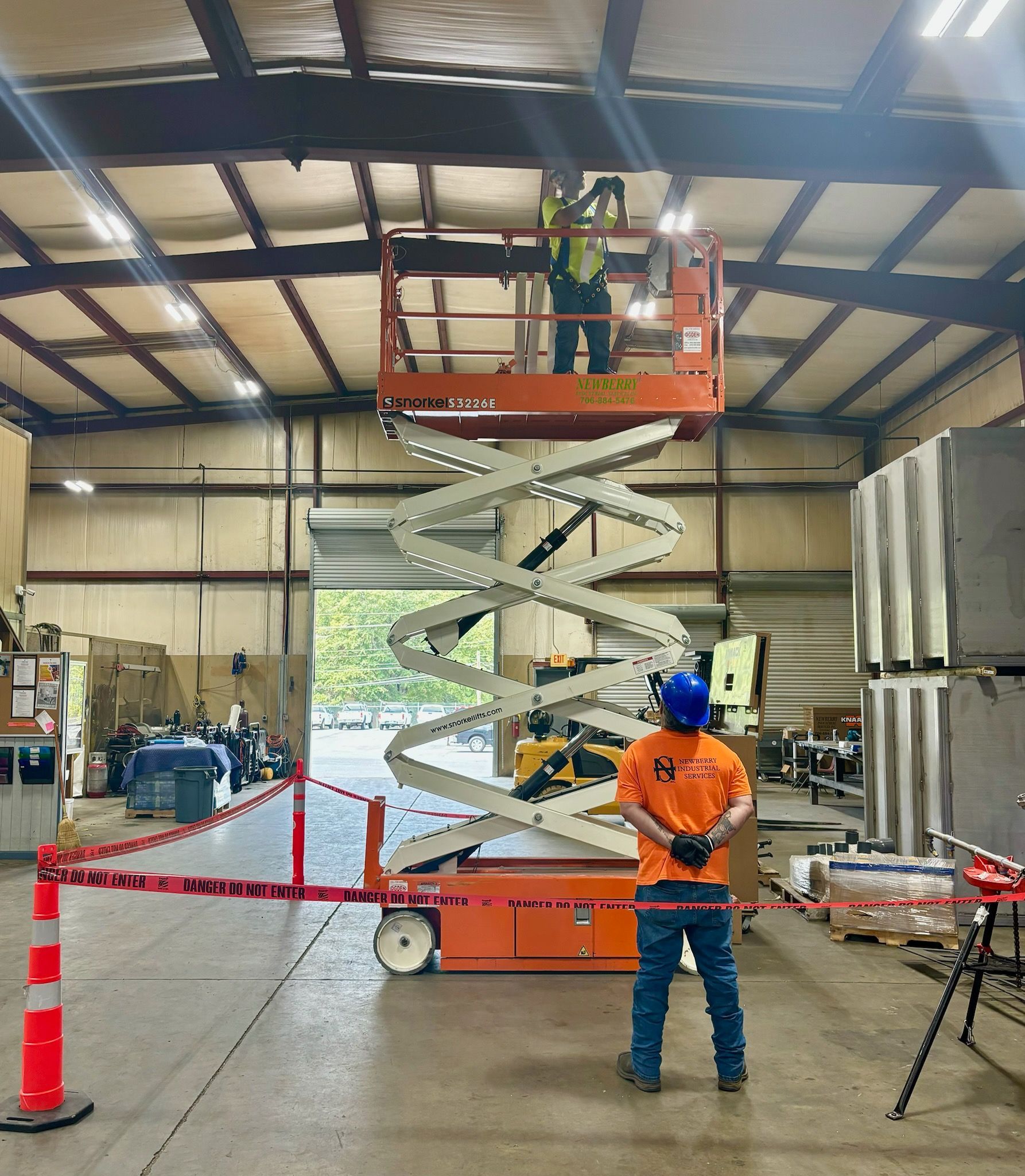 A man is standing in front of a scissor lift in a warehouse.