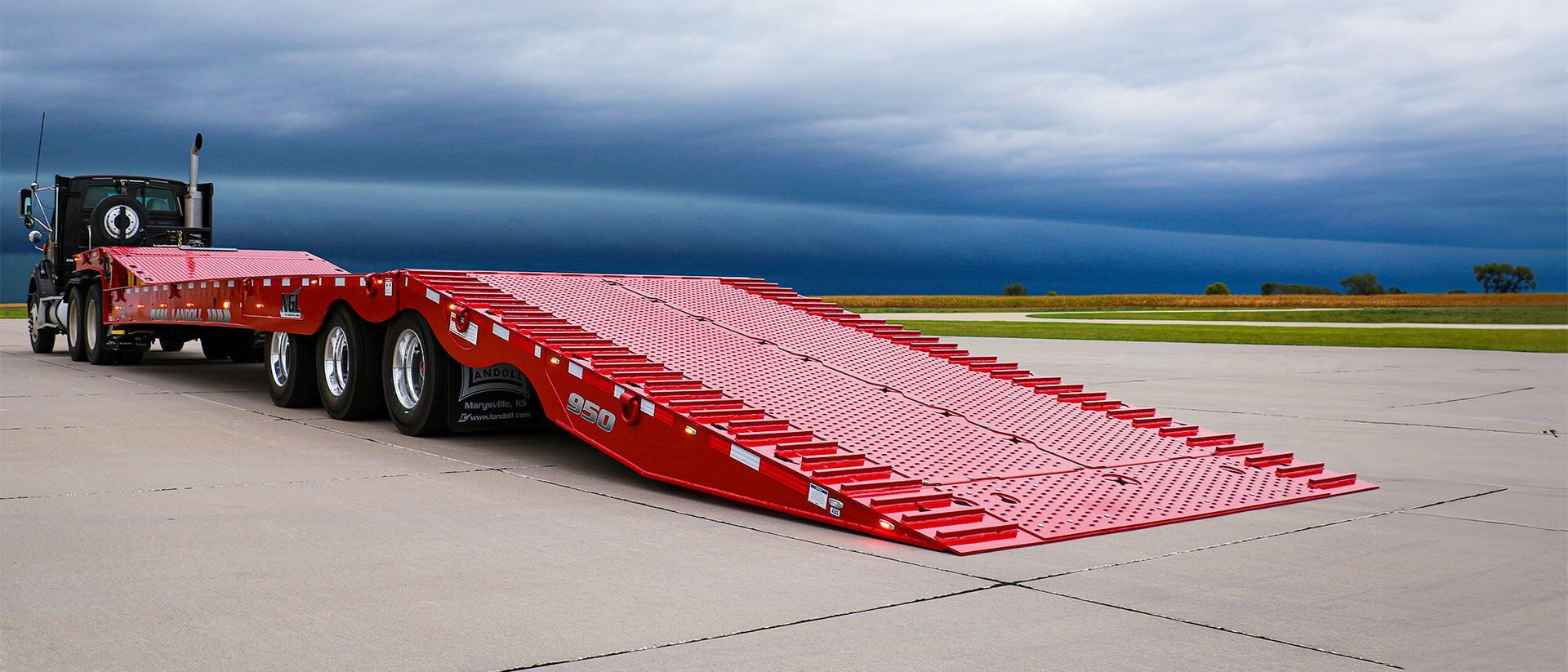 A red semi truck with a ramp attached to it is parked on the side of the road.