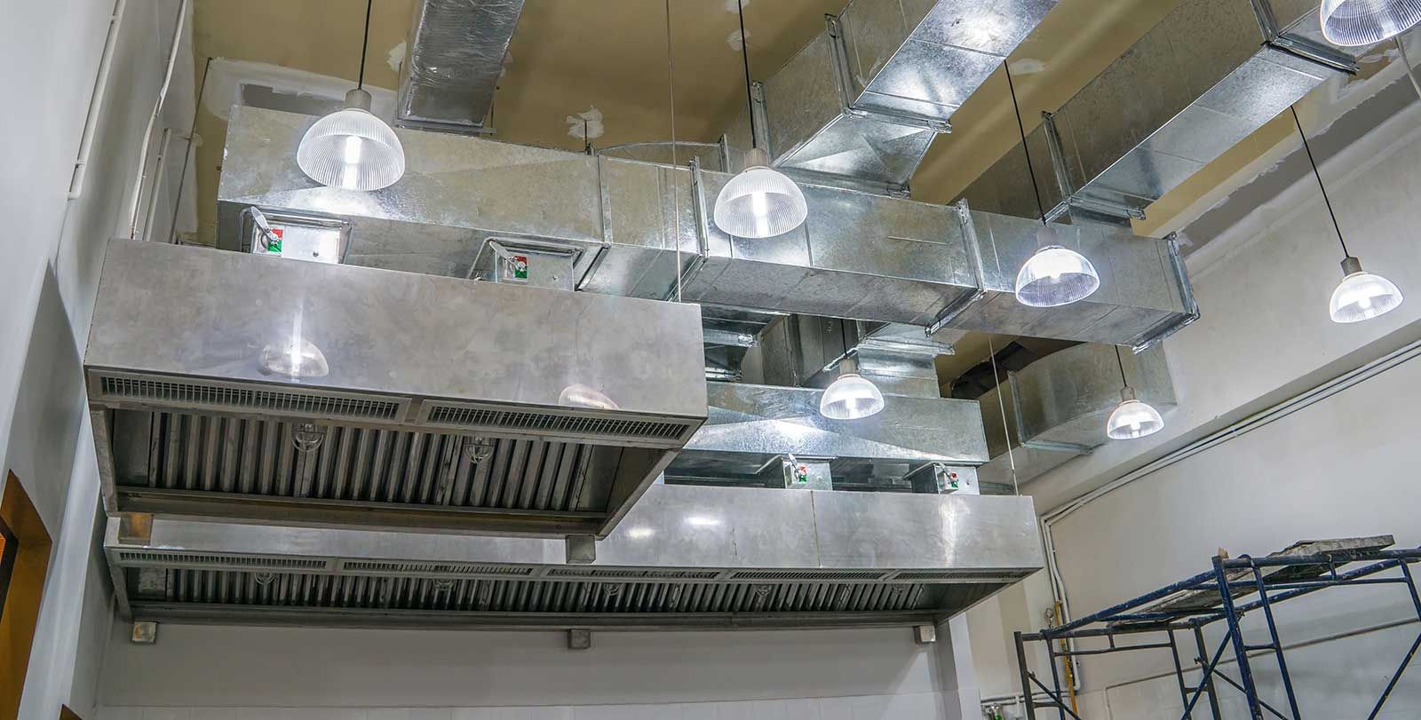 A kitchen with a lot of ventilation pipes hanging from the ceiling.