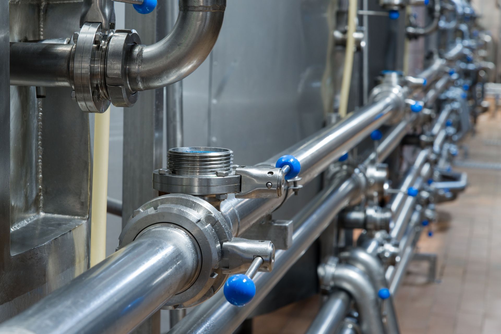 A row of stainless steel pipes with blue valves in a factory.