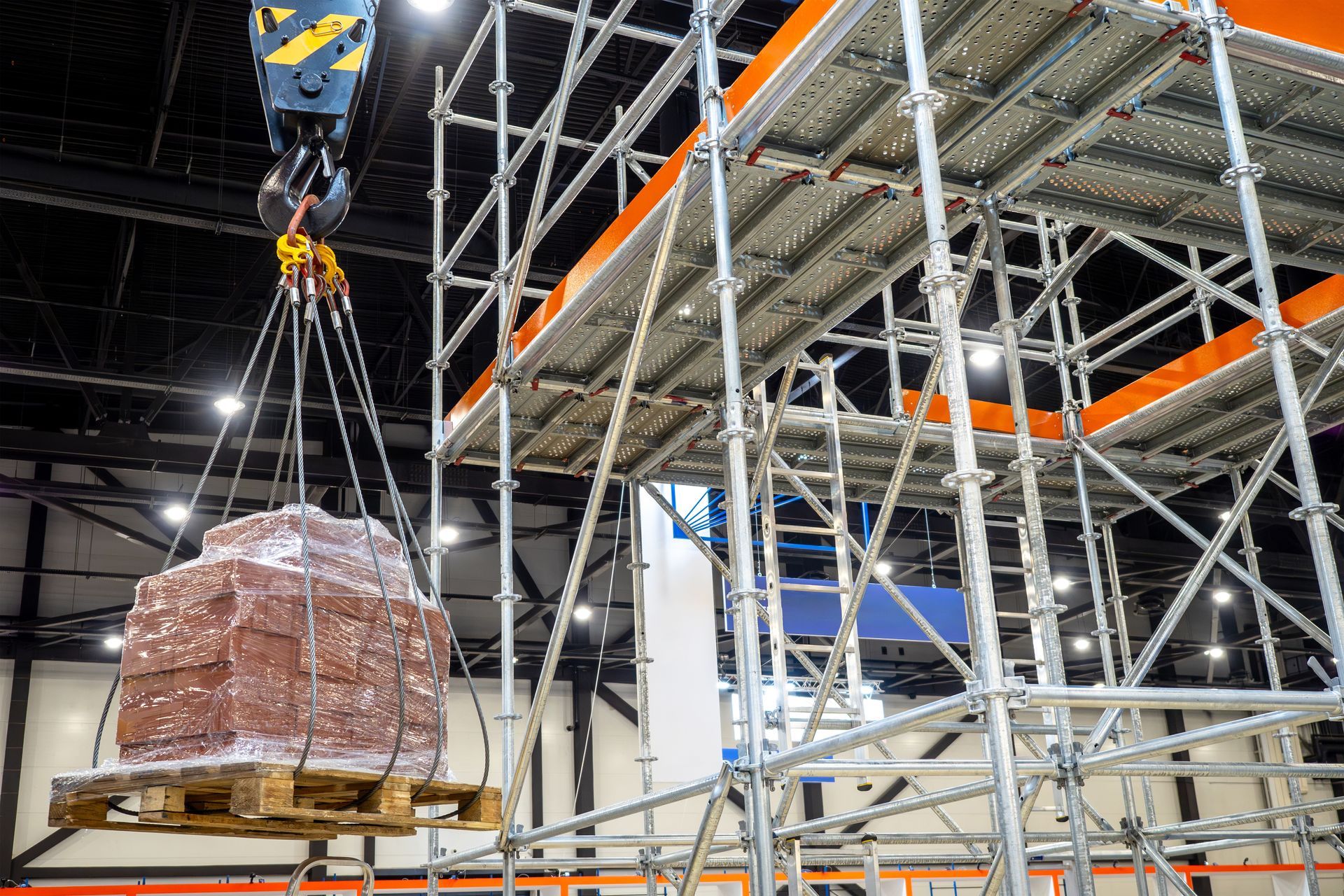 A crane is lifting a pallet of bricks over a scaffolding structure.