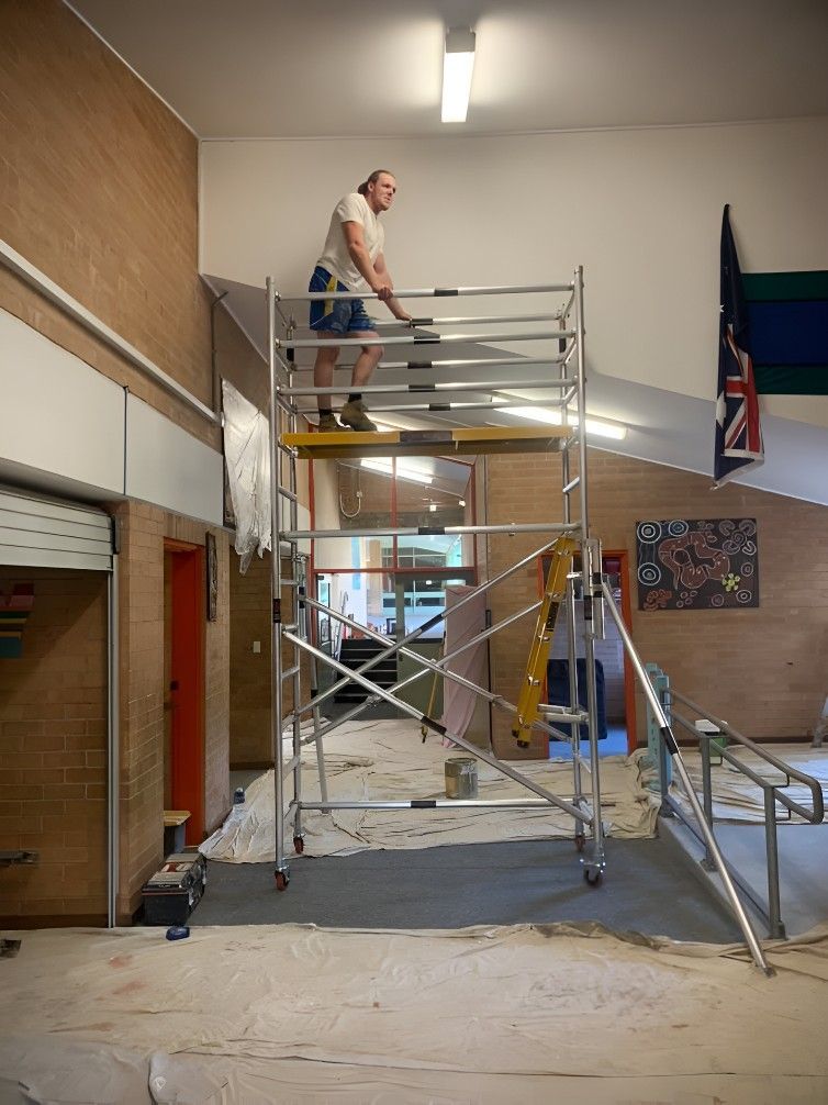 A Man is Standing on a Scaffolding in a Room — Let's Paint & Decorate Pty Ltd in Bowral, NSW