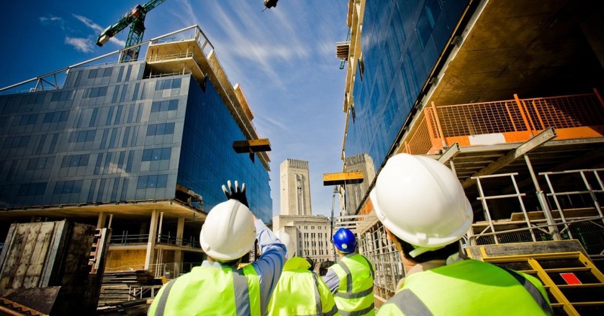Construction workers in safety vests and hard hats on a building site, pointing at a structure under construction.