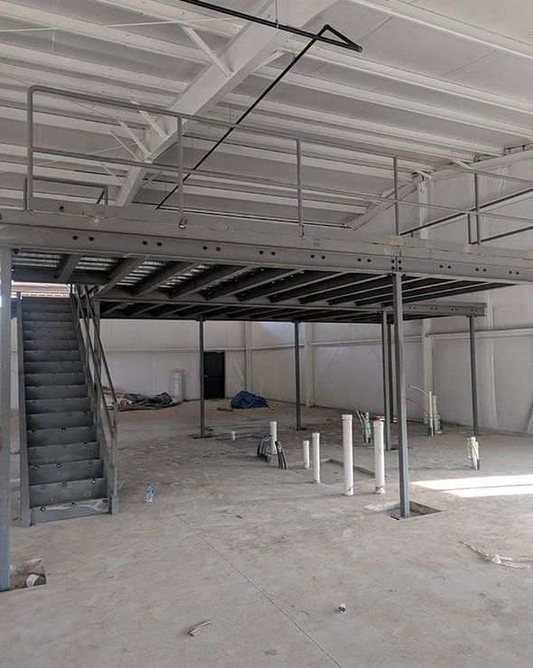 Interior view of a construction site with a steel staircase and a partially constructed mezzanine level.
