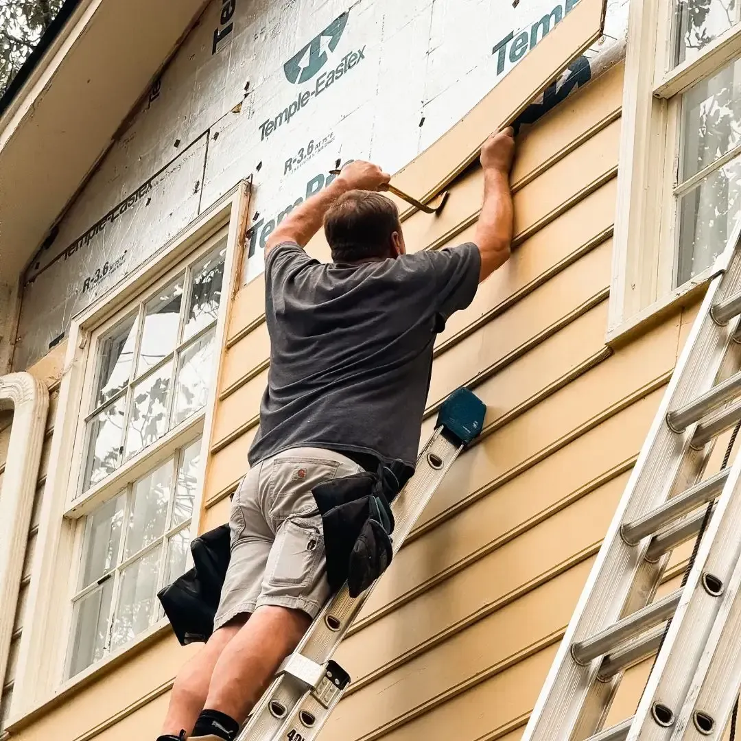 Man on a ladder installing siding on a house, exterior wall, construction.
