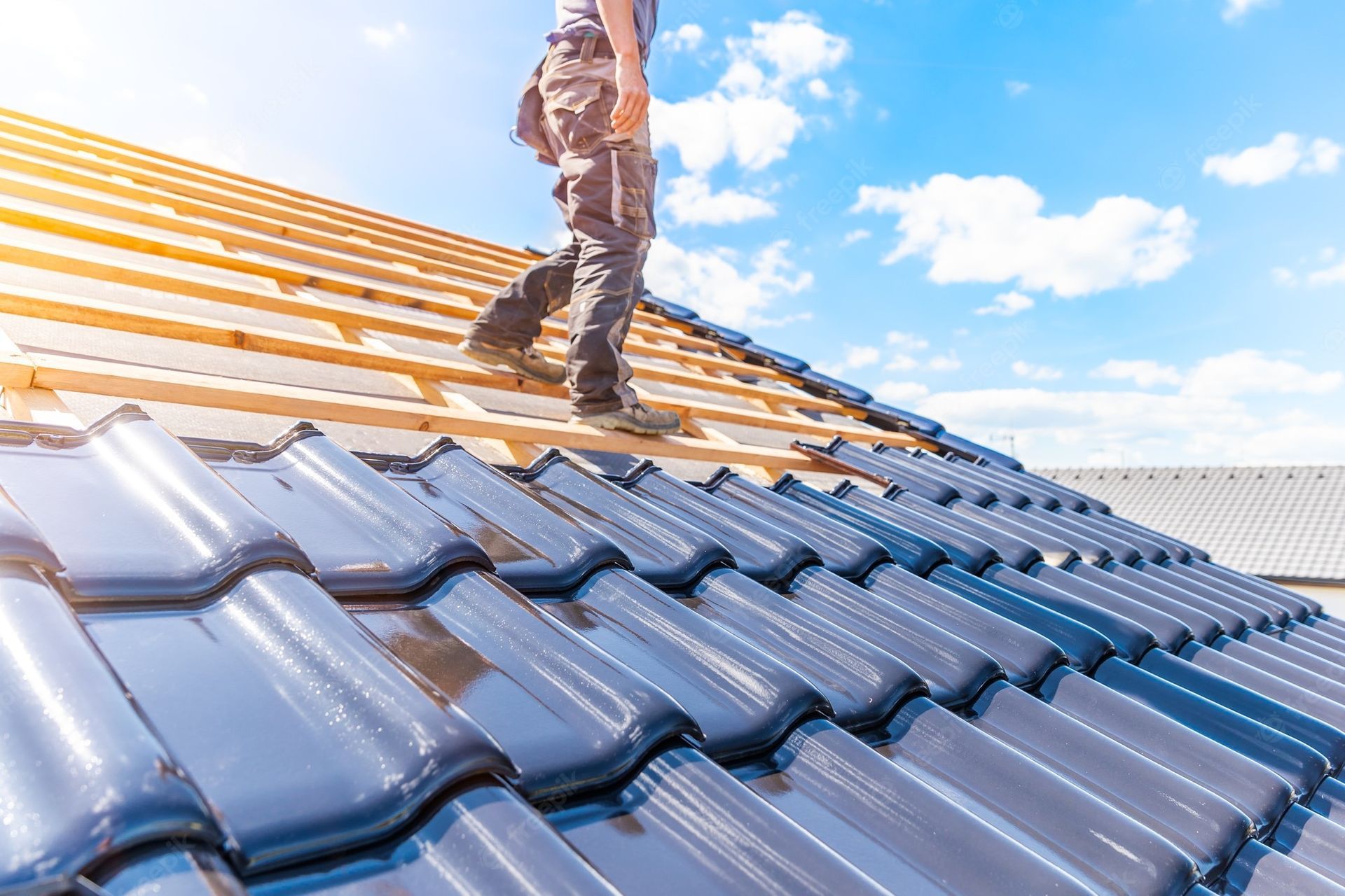 Roofer walking on new blue tile roof under a bright, sunny sky.