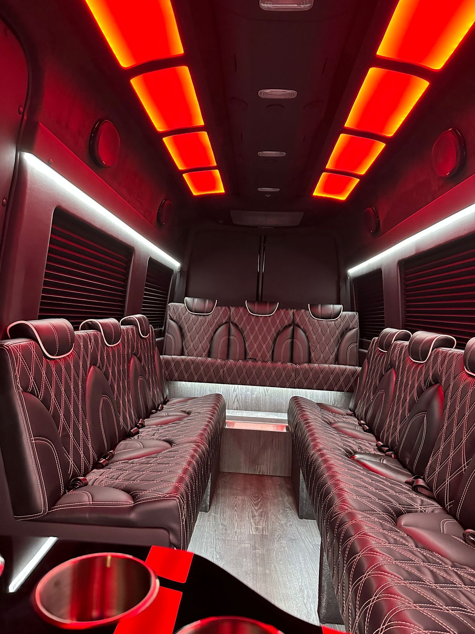 The interior of a luxury limousine van with red patterned leather seats, ambient orange ceiling lights, and cup holders.