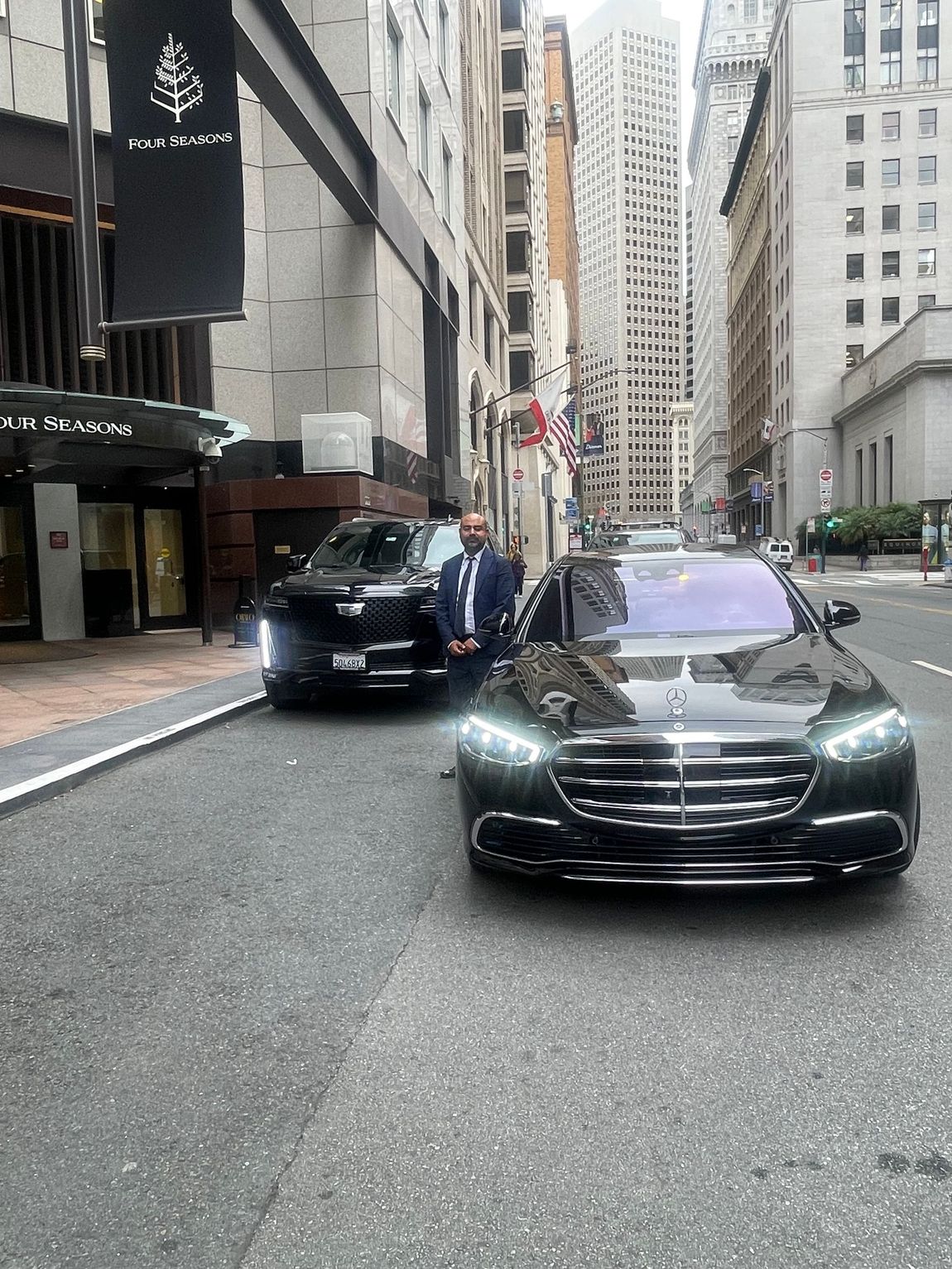A black Cadillac SUV is parked in a bike lane on a city street, partially obstructing the path behind traffic bollards.