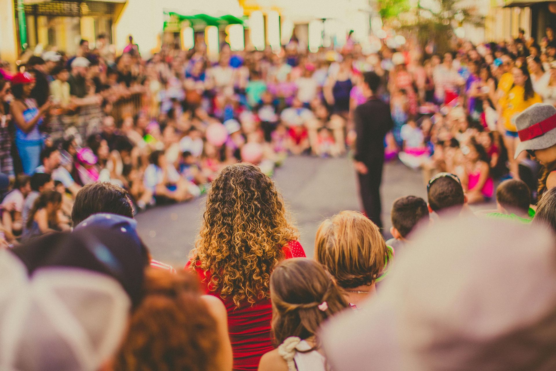 A crowd of people gathers in a street to watch a performer standing in the center.
