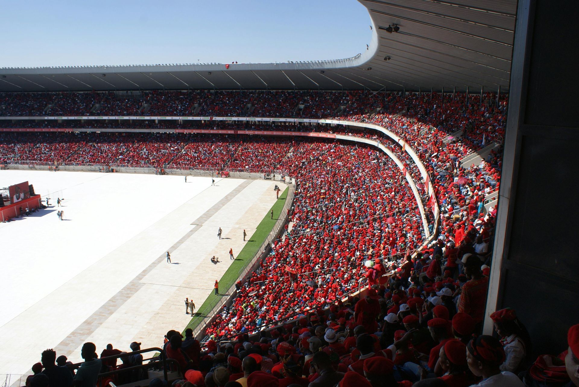 A crowded stadium with fans wearing red clothing filling the stands around a large white field.
