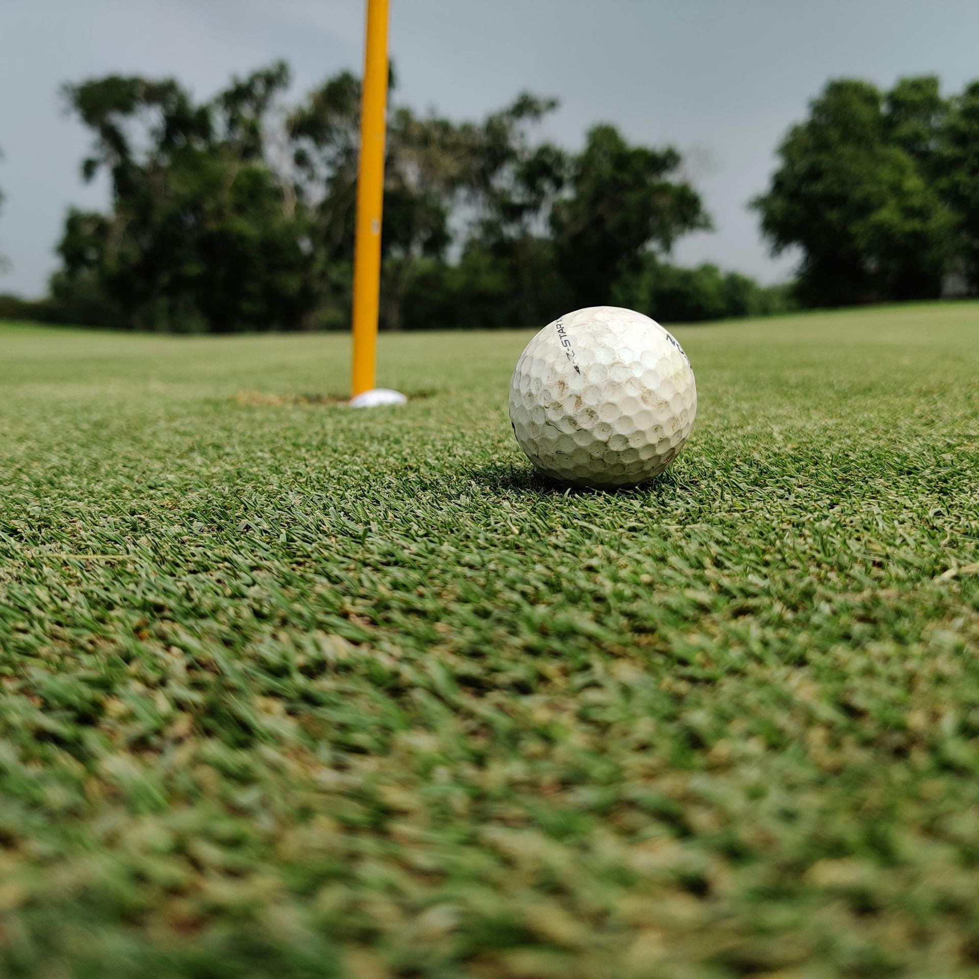 A golf ball sits on a green, positioned just inches away from a hole marked by a yellow flagstick.