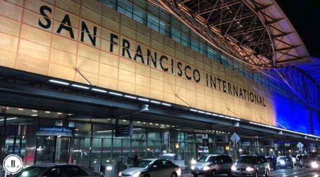 The San Francisco International Airport terminal exterior at night, with vehicles driving past the illuminated building.