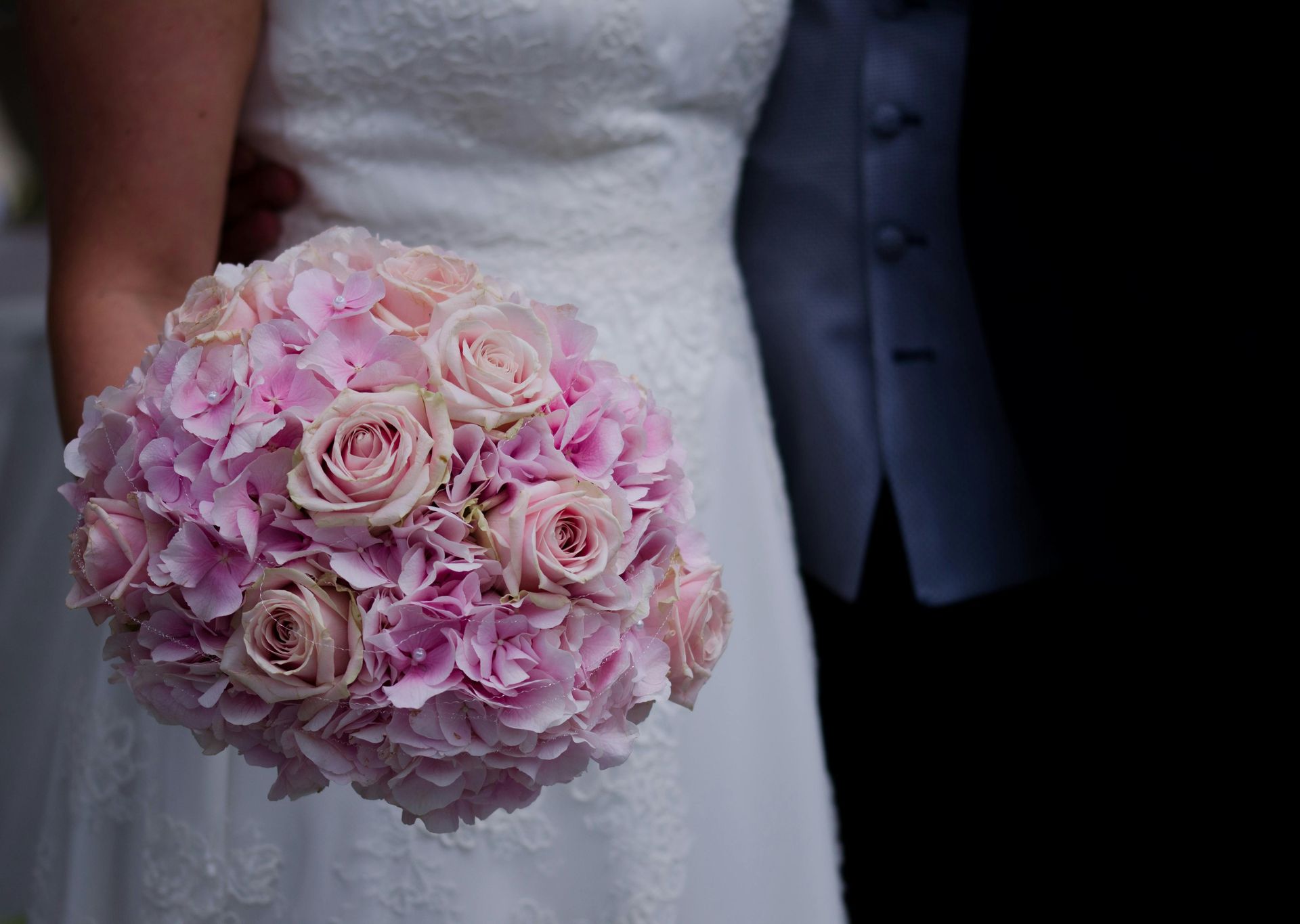 A bride holding a round wedding bouquet of soft pink roses and light purple hydrangea flowers.