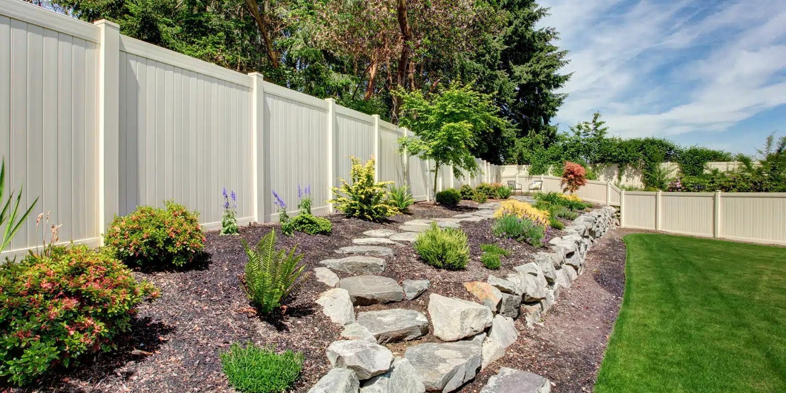 A white fence surrounds a garden with rocks and plants.
