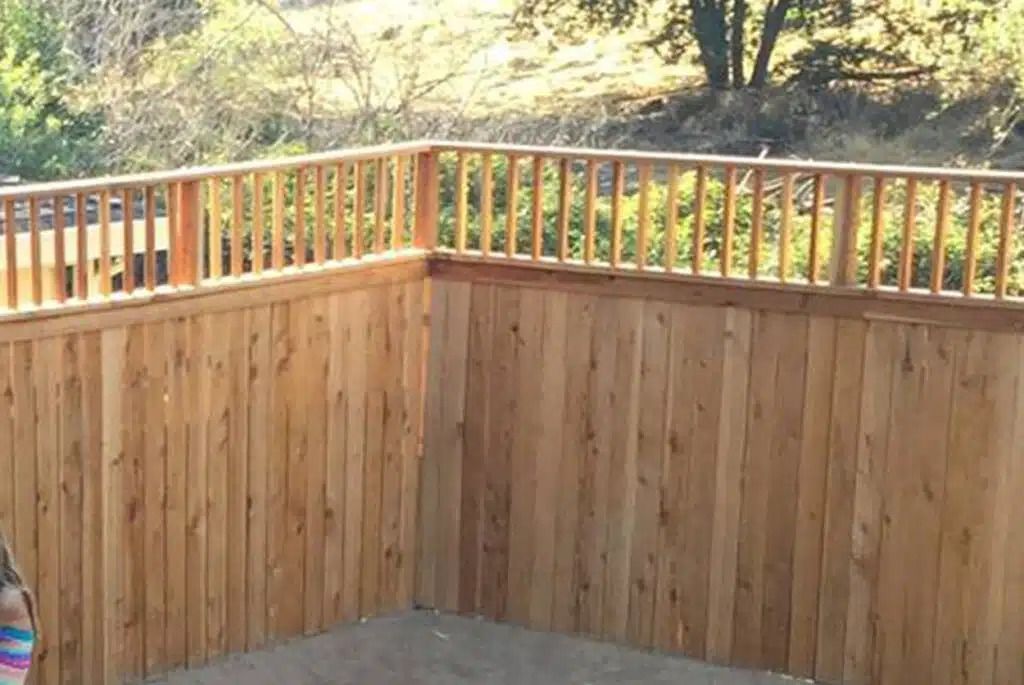 A little girl is standing on a deck with a wooden railing.
