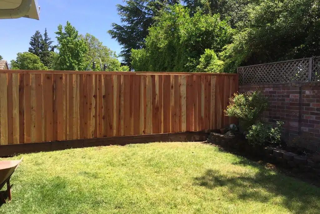 A wooden fence surrounds a lush green lawn in a backyard.
