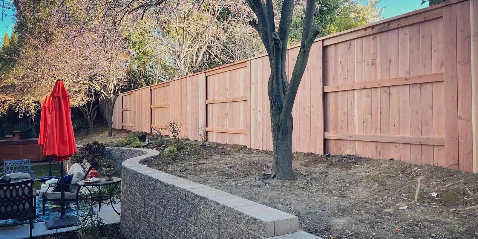 A wooden fence surrounds a patio area with a red umbrella.