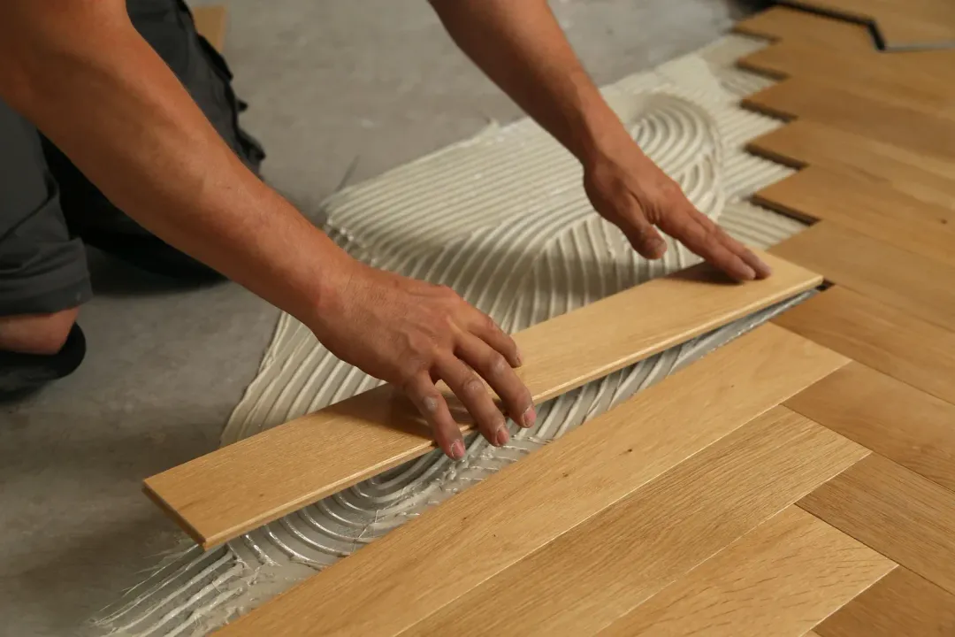 A person is laying a piece of wood on the floor