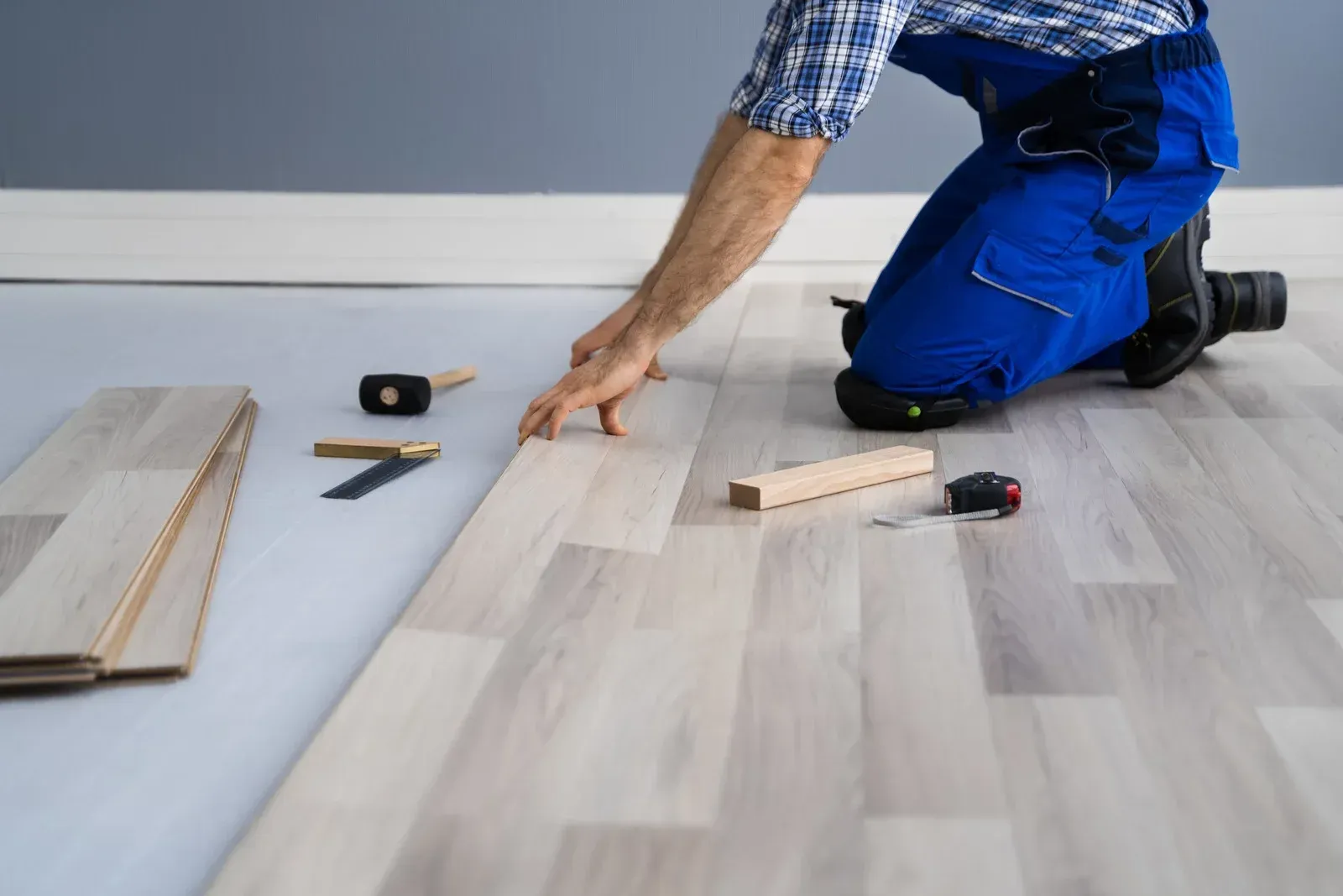A man is kneeling down to install a wooden floor.