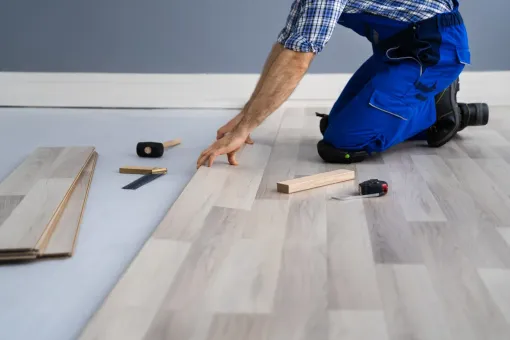 A man is kneeling down to install a wooden floor.