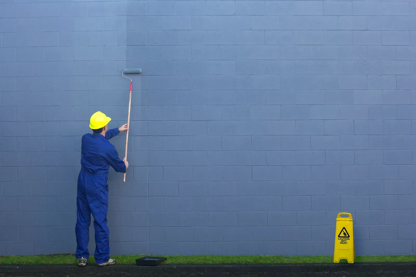 A man is painting a blue wall with a roller.