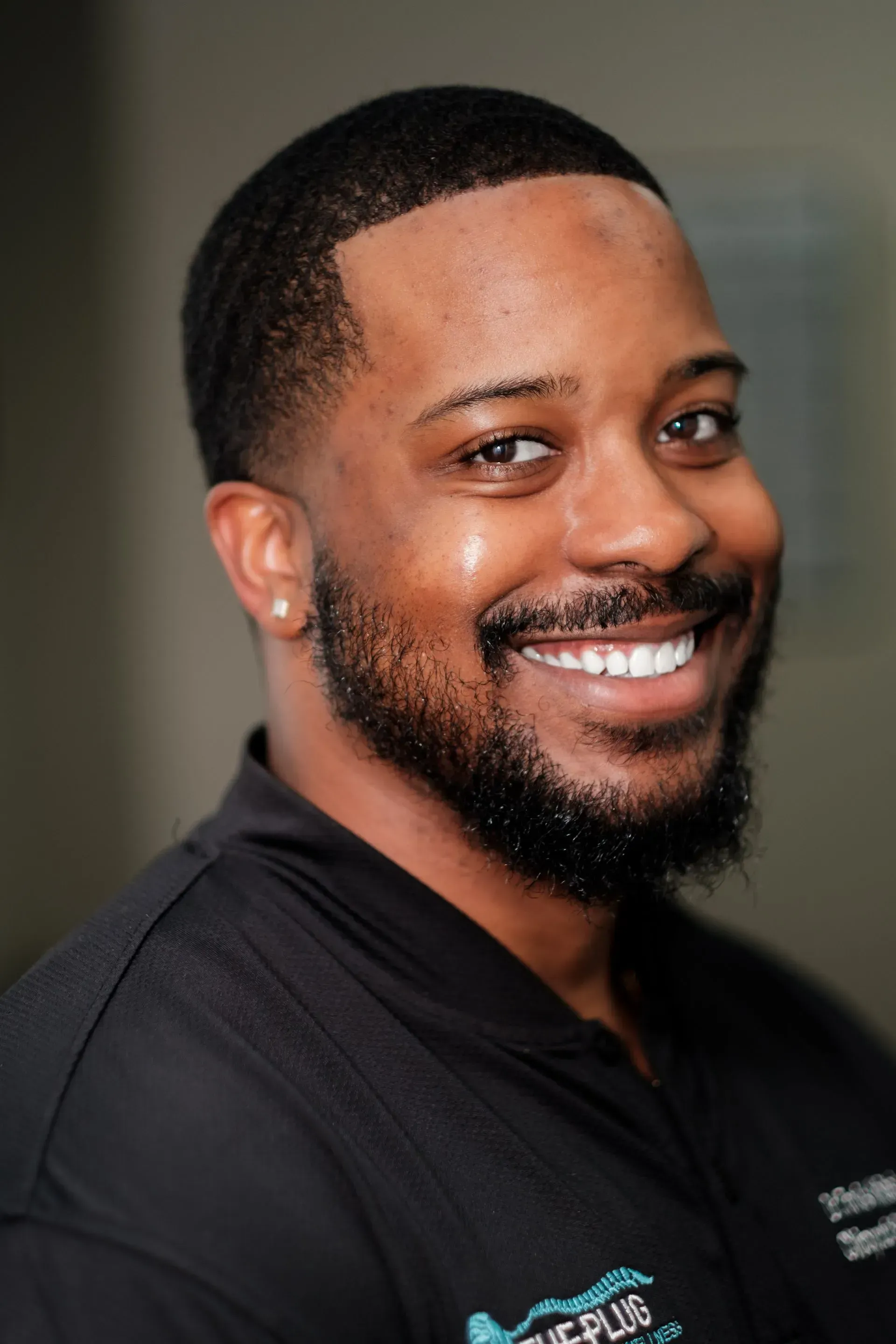 Dr. Travis, a Black man with crossed arms, smiles at the camera. He wears a white polo shirt and a watch.