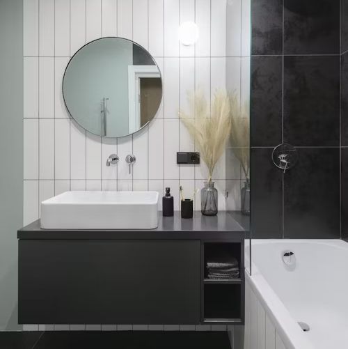 Modern bathroom with white and black tiles, floating vanity, round mirror, and a bathtub.