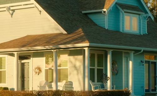 A blue and white house with a porch and chairs on it.