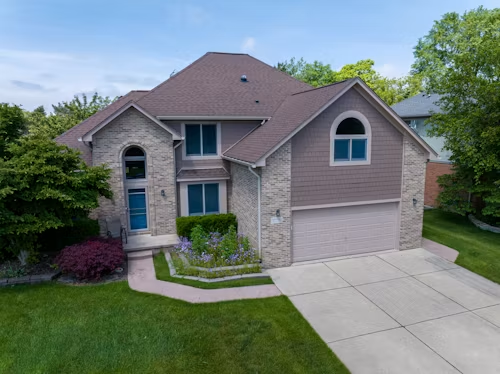 Suburban two-story brick house with attached garage, blue front door, and manicured lawn