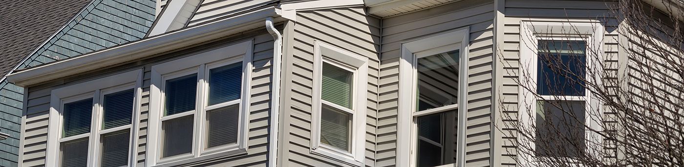 A section of a house exterior with several windows and siding in a daylight setting.