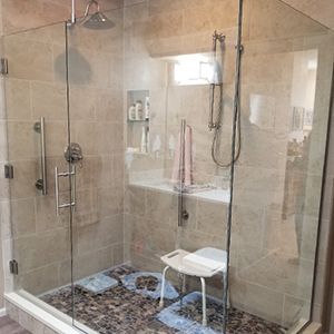 A bathroom with a walk in shower with a glass door and a stool.