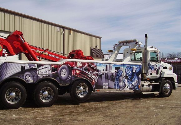 White tow truck with colorful graphics parked near a building on a sunny day.