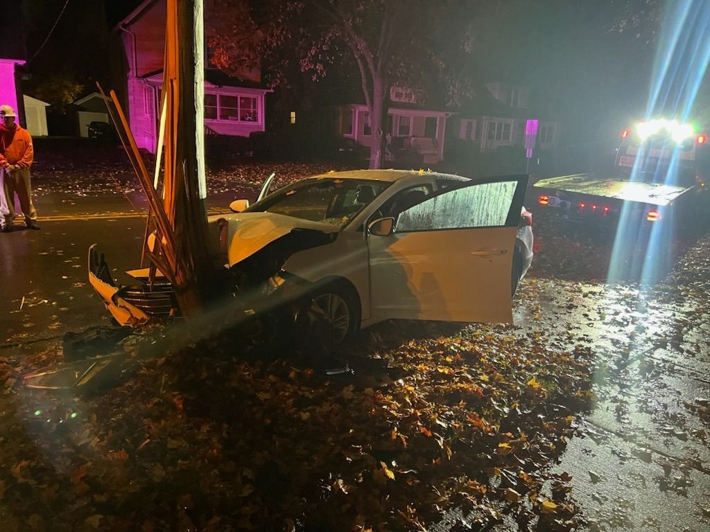 Car crashed into a utility pole at night. Damaged car, fallen pole, tow truck in the background.