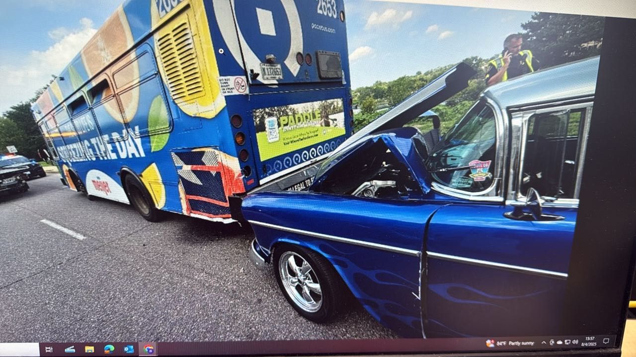 Blue classic car crashed into a bus on a road. The bus is blue and yellow.