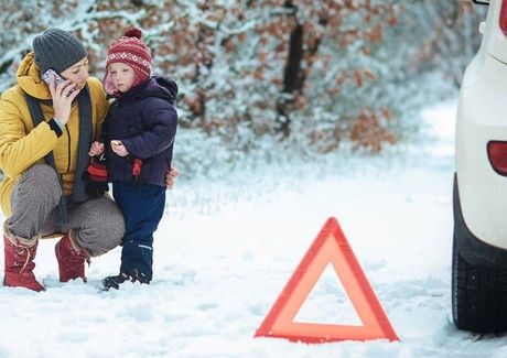 Woman and child beside a broken-down car in snowy woods; woman calls for help near a warning triangle.
