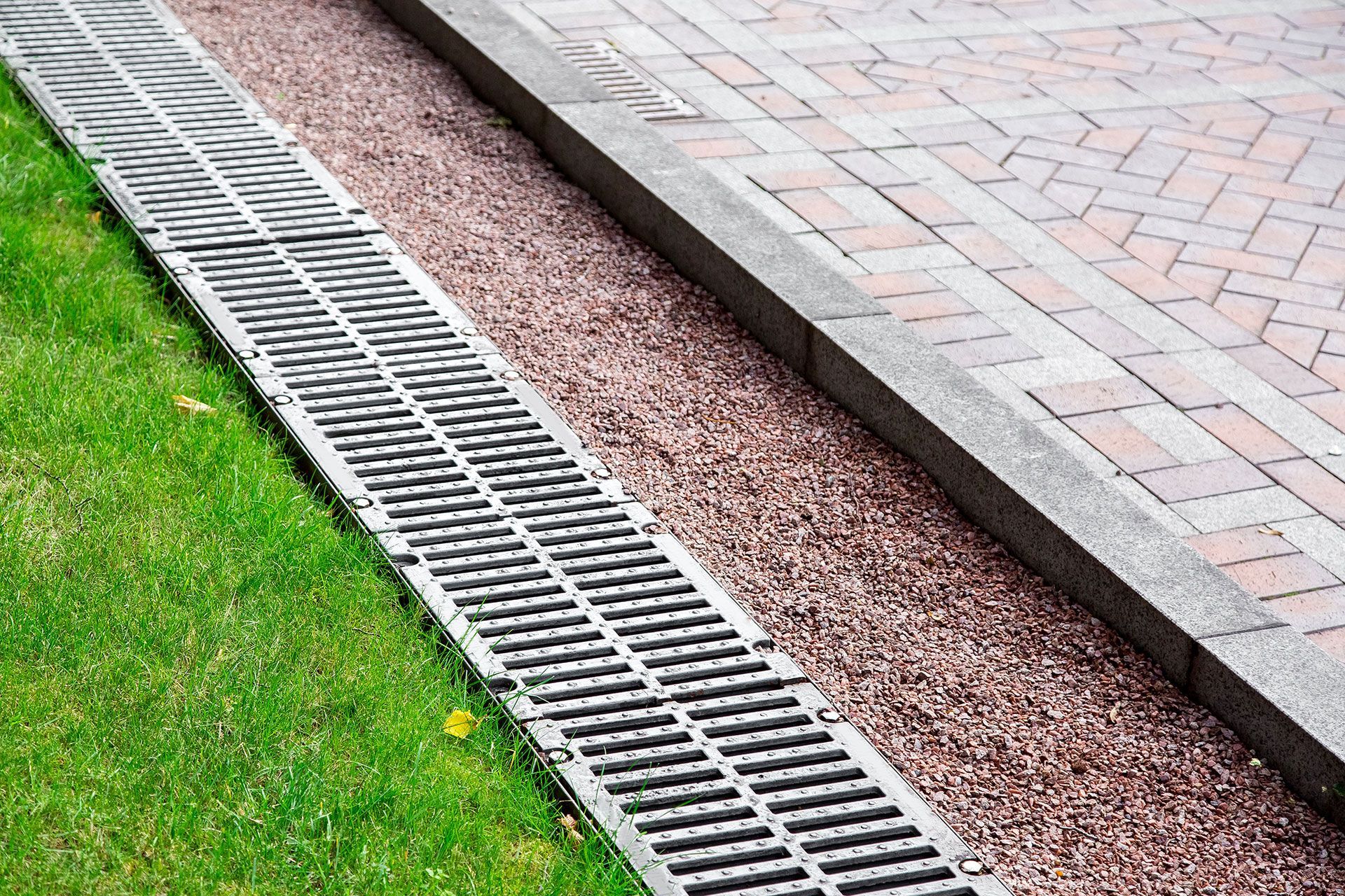 drainage system in the park between green grass and stone pavement, drainage grate and pebbles