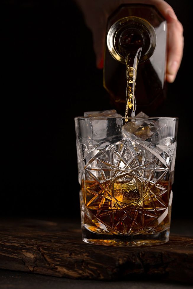 A person is pouring whiskey into a glass with ice.