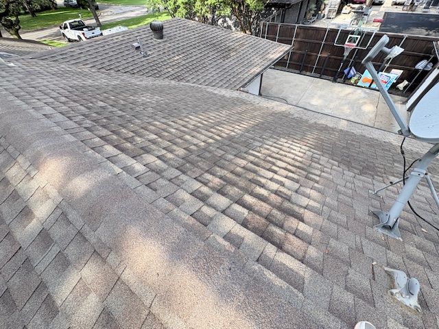 Roof shingles under repair on a house, with a worker and equipment visible near the edge