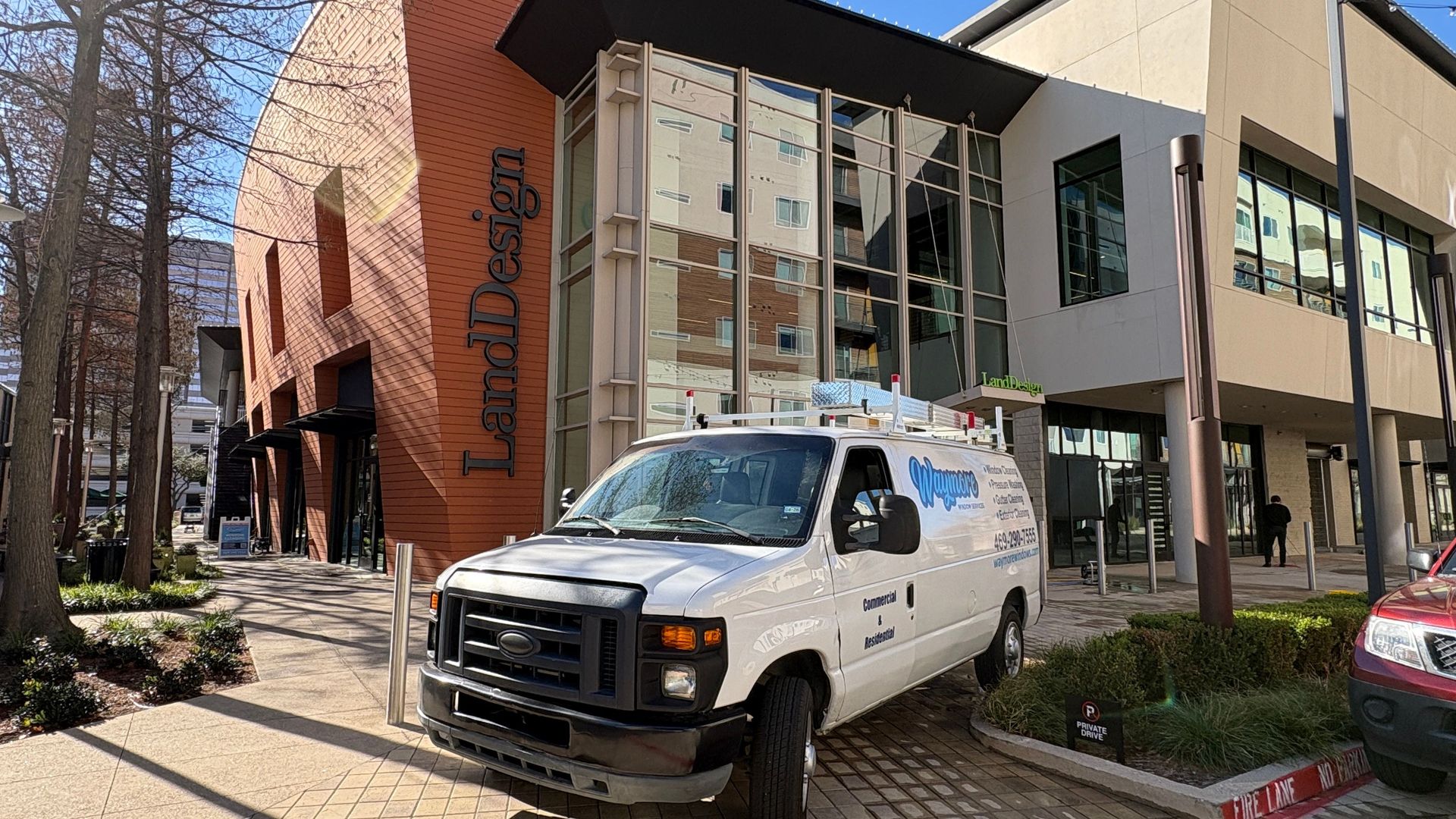 A white service van is parked on a brick-paved sidewalk in front of a modern building labeled "LandDesign."