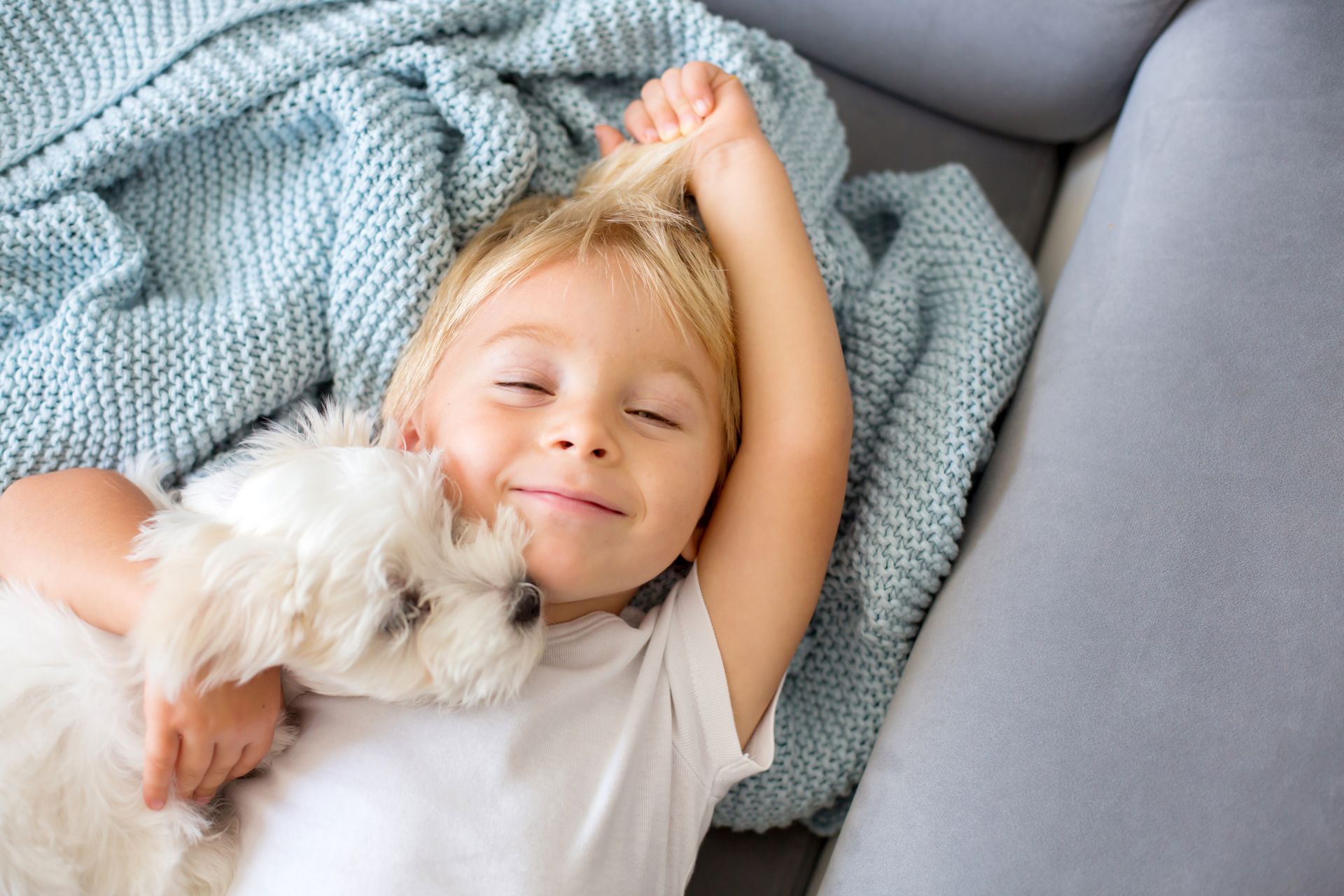 A little boy is lying on a blanket holding a puppy