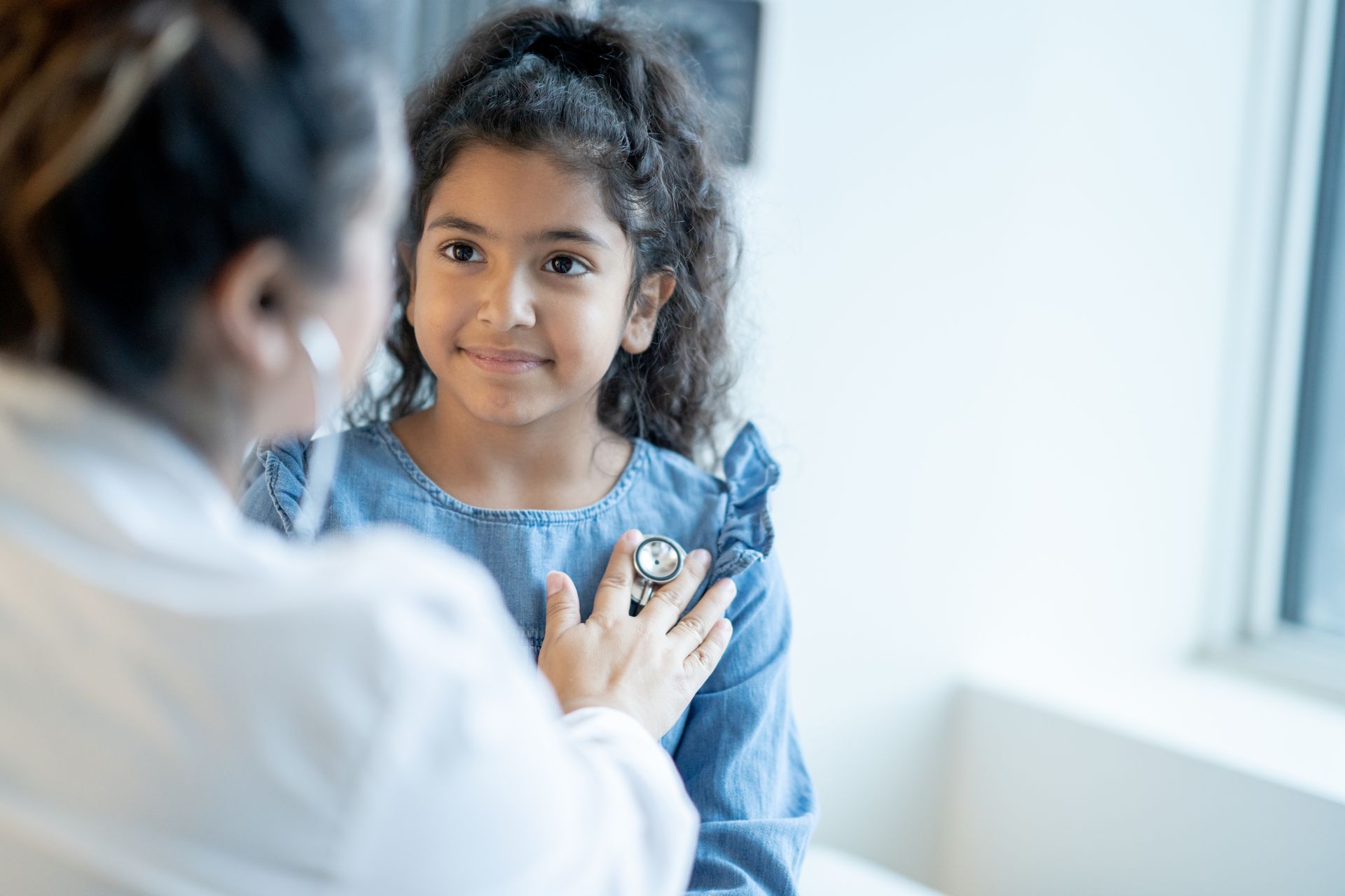 A pediatrician is listening to a girl's heart with a stethoscope