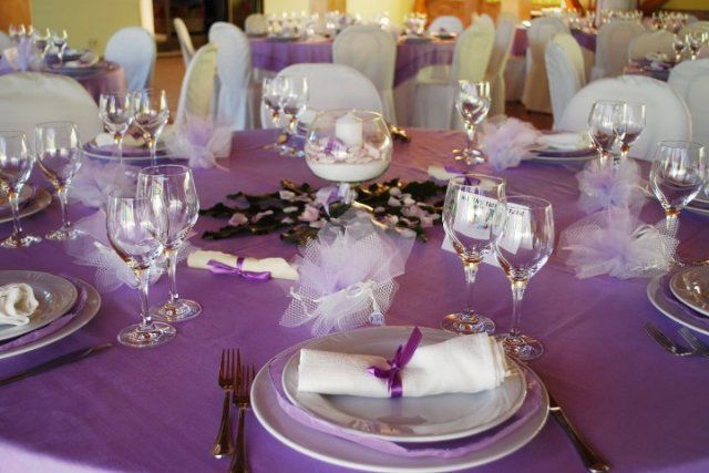 Un tavolo è apparecchiato per un ricevimento di nozze con piatti e bicchieri viola.