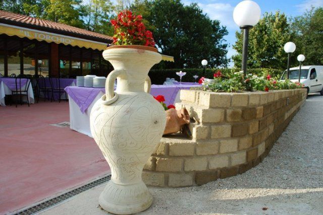 Un grande vaso con dei fiori è appoggiato accanto a un muro di mattoni.