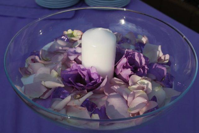 Una ciotola di vetro piena di fiori viola e una candela bianca