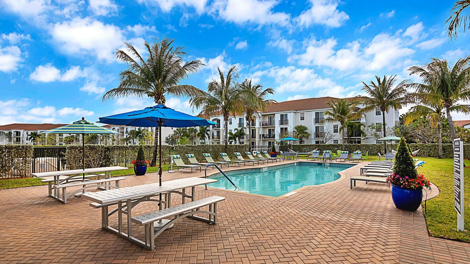 A large swimming pool surrounded by palm trees and picnic tables.
