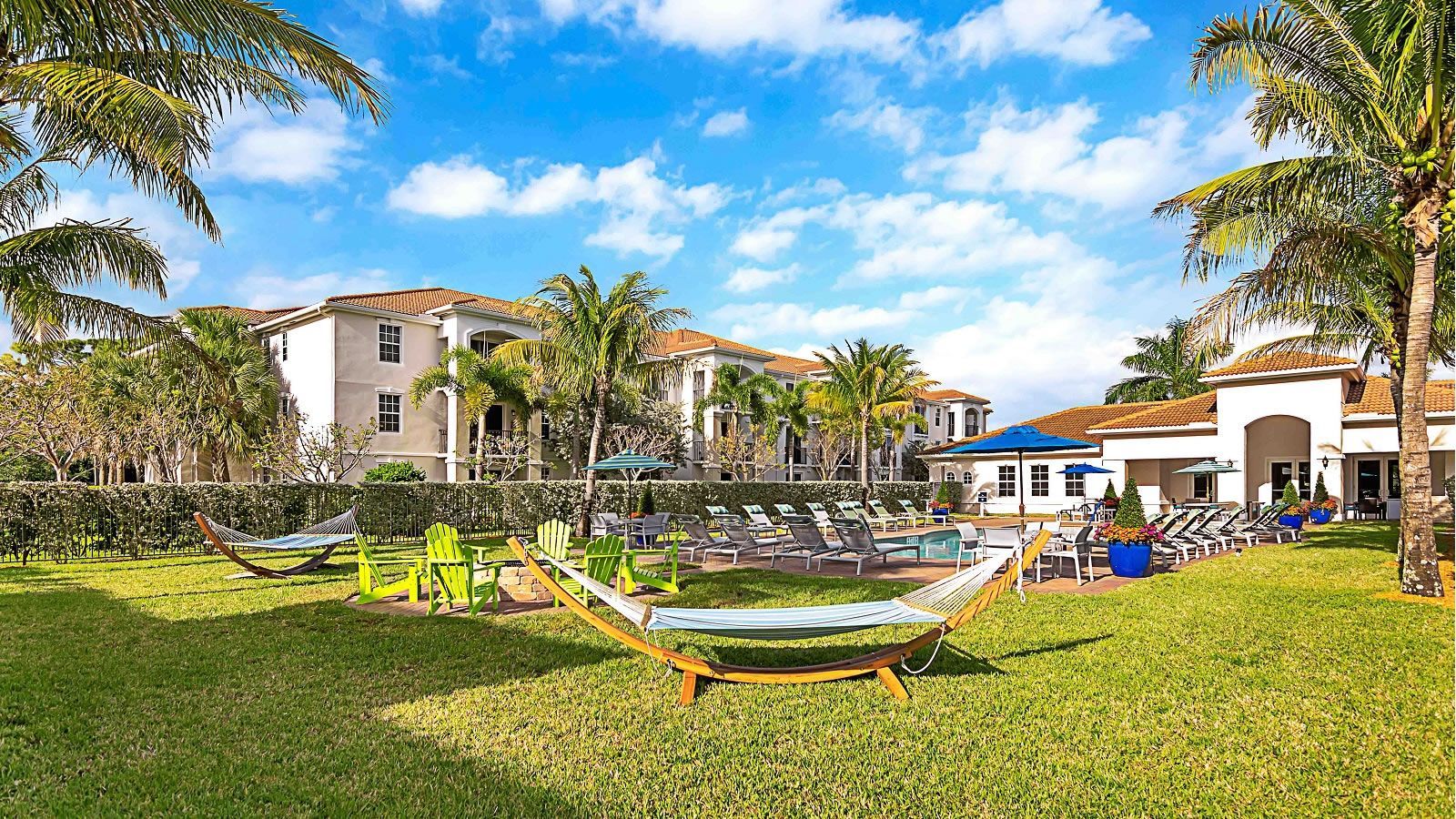 A lush green lawn with hammocks and chairs in front of a building.