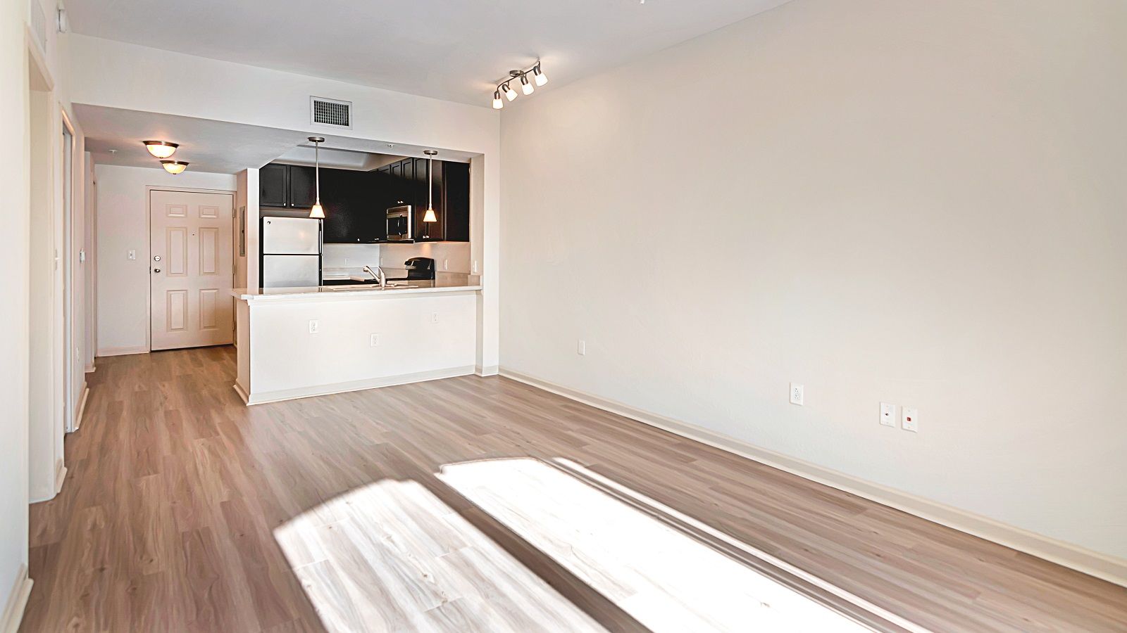 A living room with hardwood floors and a kitchen in the background.