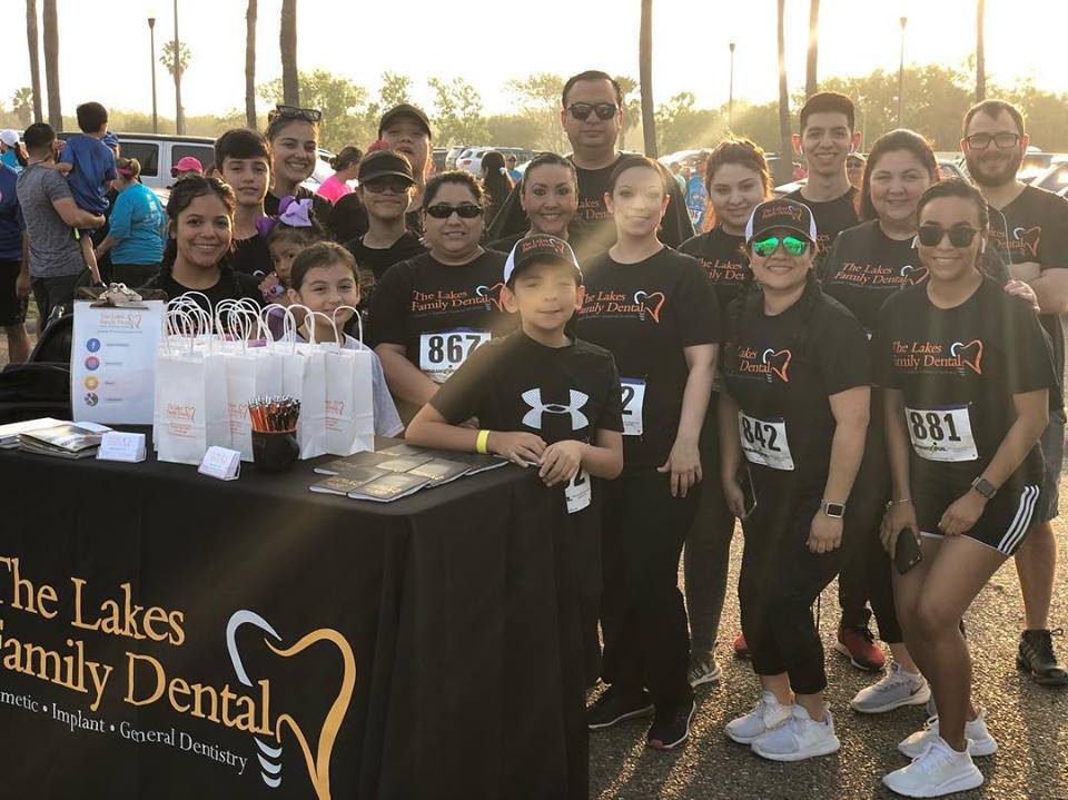 A group of people are posing for a picture in front of a table that says the lakes family dental.