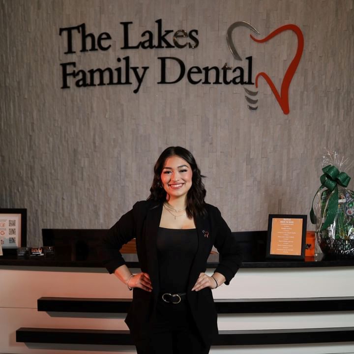 Destiny is standing in front of a sign that says the lakes family dental .