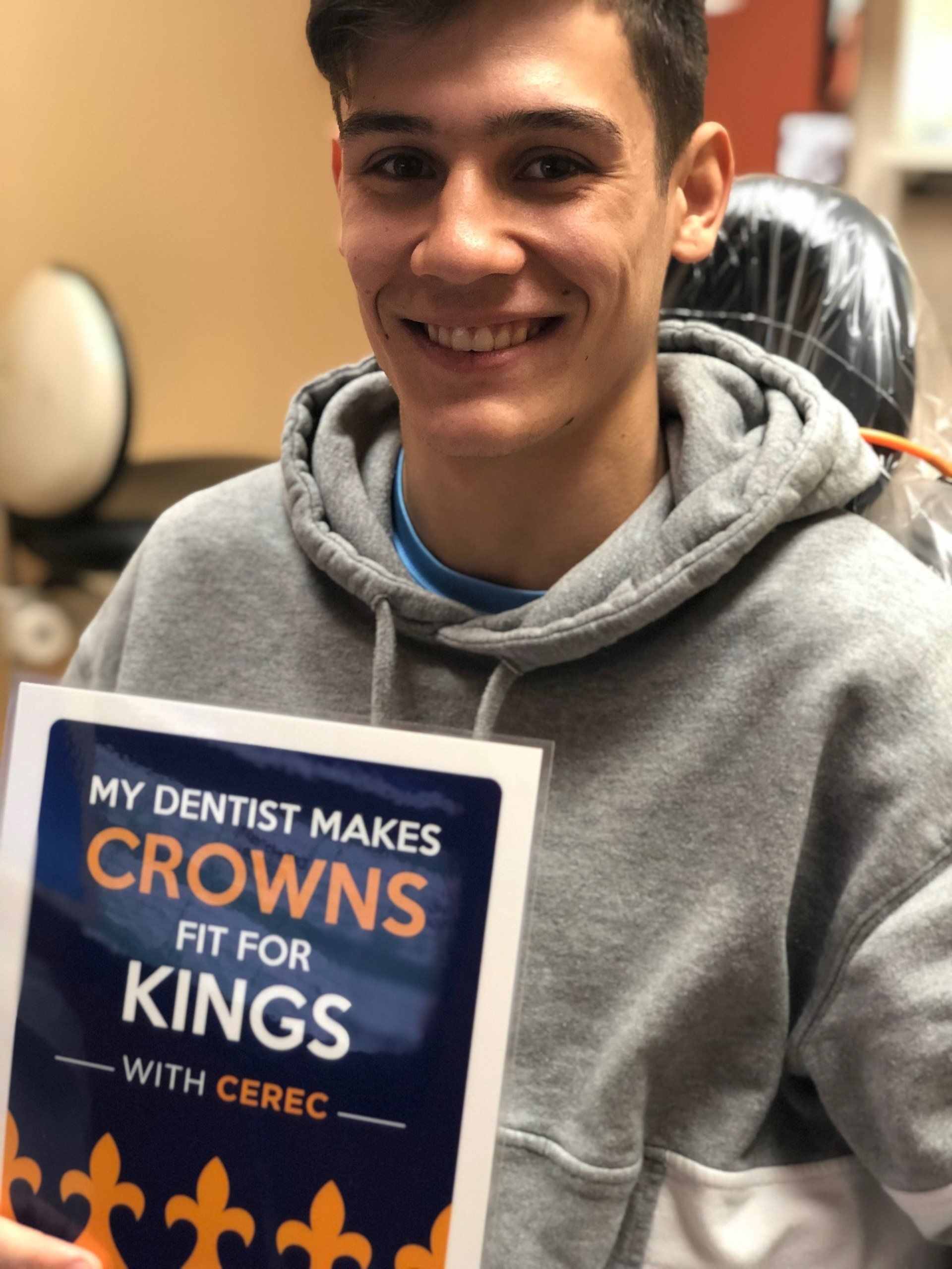 A young man is holding a sign that says my dentist makes crowns fit for kings